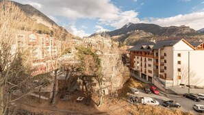 Un pueblo de montaña con edificios de varios pisos, un área de estacionamiento y vistas a montañas al fondo.