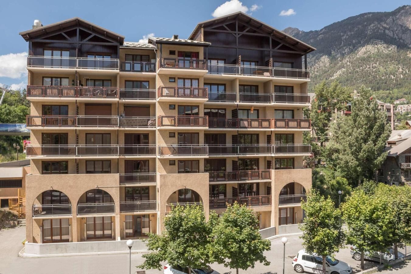 Un hôtel à plusieurs étages, doté de balcons, de fenêtres en arc de cercle et surplombant un paysage montagneux.