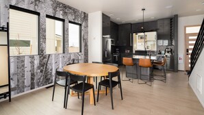 A modern kitchen with dark cabinets, a central island, and a dining area with a wooden table and chairs. - Luxury Stand Alone Condo, Minutes from Downtown Bozeman, Garage & Outdoor Patio (Bozeman)
