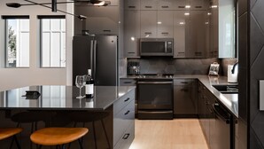 A modern kitchen with stainless steel appliances, a central island with stools, and large windows providing natural light. - Luxury Stand Alone Condo, Minutes from Downtown Bozeman, Garage & Outdoor Patio (Bozeman)