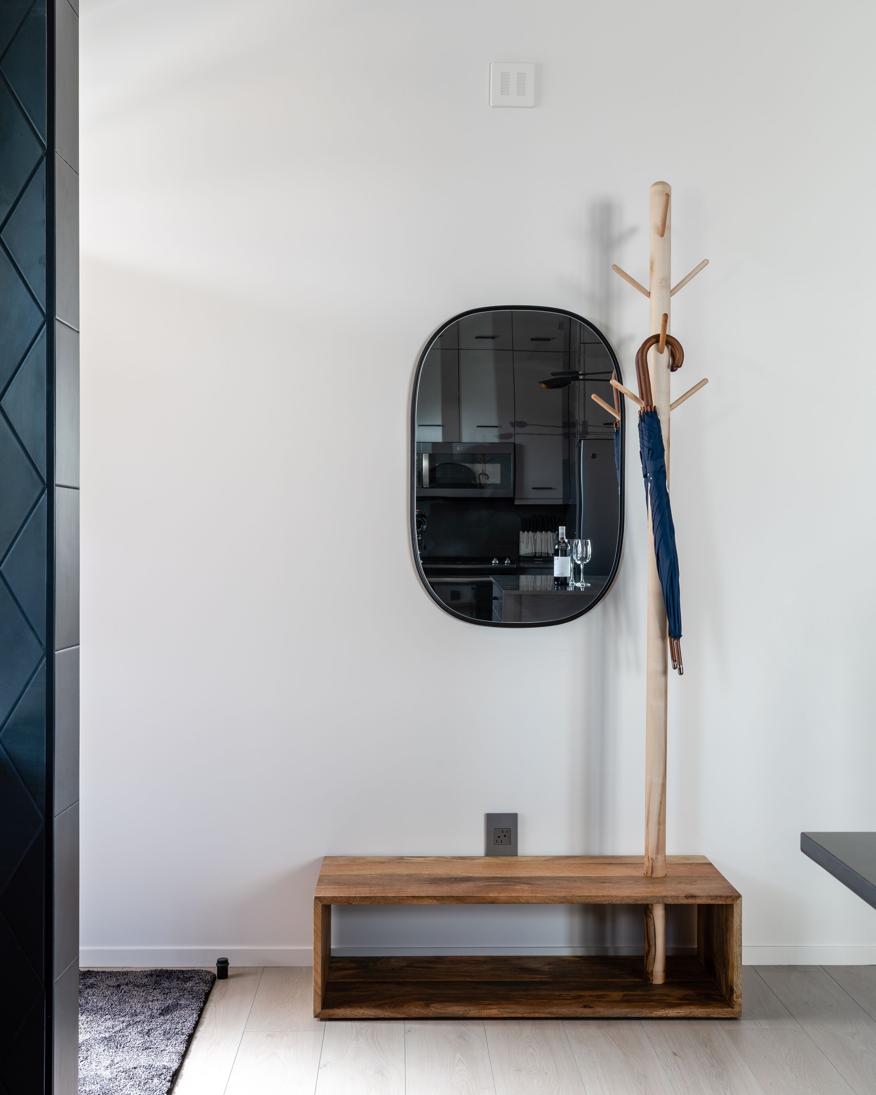 A modern interior with a wooden bench, a coat rack with an umbrella, and a round mirror on the wall.