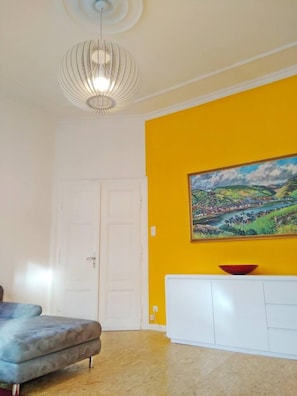 Um quarto com porta branca, um sofá, um armário branco e uma pintura de paisagem na parede amarela.