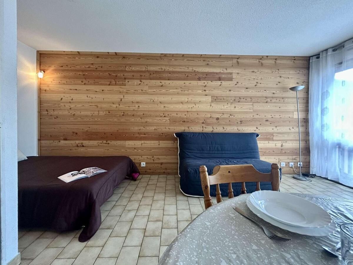 Ein Zimmer mit einer Holzvertäfelung, einem Bett, einem blauen Sofa, einem Esstisch mit Teller und Besteck sowie einer Stehlampe.