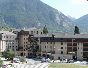 A multi-story hotel with a parking lot in front, surrounded by mountains.