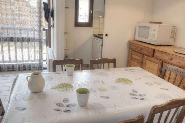 A dining area with a table set for two, a microwave, and a wooden cabinet.