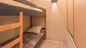 Een kleine, smalle kamer met een stapelbed en een enkel bed.