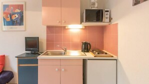 Een kleine keuken met pastelroze kastjes, een magnetron, een spoelbak en een klein fornuis.