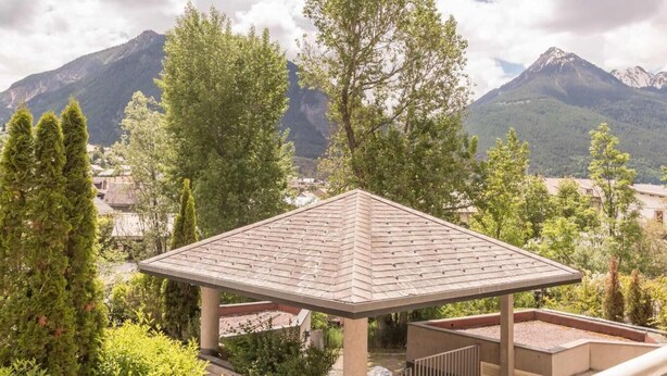 Un gazebo con tetto in tegole, immerso nel verde e con vista su un paesaggio montuoso.