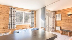 Un espace repas comprenant une longue table, des chaises et une fenêtre avec des rideaux.