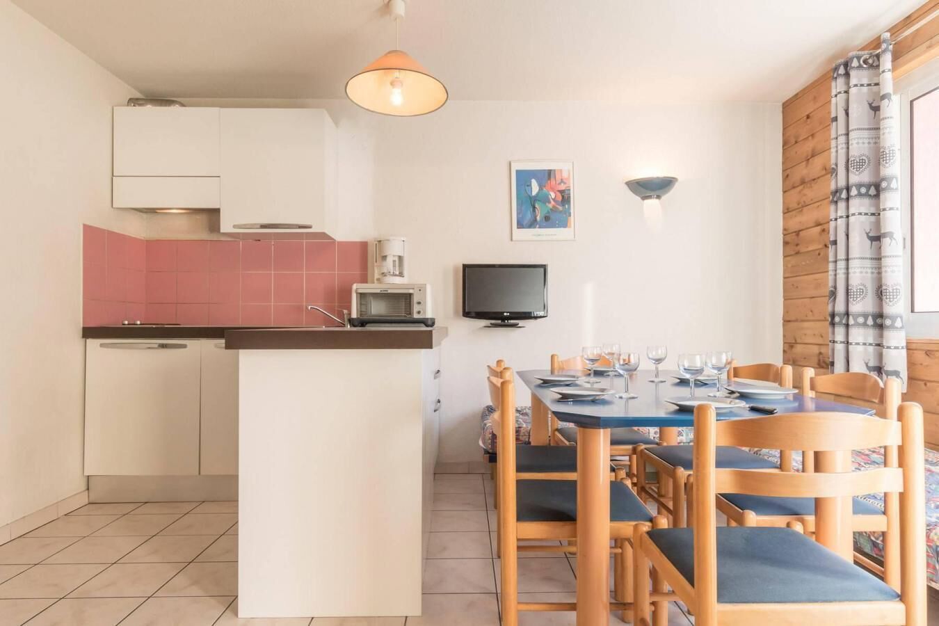A compact kitchen with a microwave, toaster, and coffee maker. There is a dining table with chairs and a TV mounted on the wall.