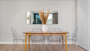 Ein Essbereich mit einem Holztisch, vier transparenten Stühlen, einer Vase mit getrocknetem Pampasgras und einem großen Spiegel an der Wand.