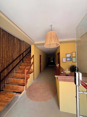 A hallway with a wooden staircase, a woven pendant light, a reception desk, and framed certificates on the wall. - Pousada Numei de Jeri (Jijoca de Jericoacoara)