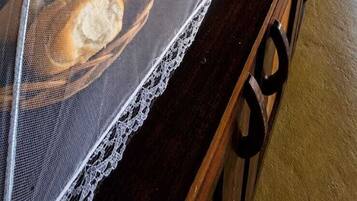 A long wooden counter with bread baskets covered by mesh, a woven wall hanging, and a rustic ceiling.