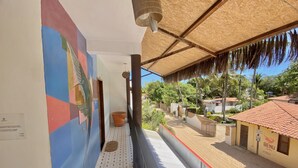 Ein schmaler Balkon mit Fliesenboden, einer Wandmalerei und Blick auf ein Wohngebiet mit Häusern und Palmen.