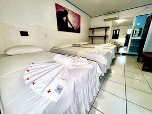 Une chambre d’hôtel avec trois lits, chacun agrémenté de draps blancs et de motifs floraux rouges, un tableau au mur et un sol carrelé.