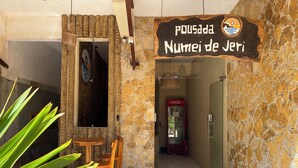 Ein Eingang mit Steinwänden, ein Kühlschrank von Coca-Cola, ein Holztisch und Stühle sowie ein Schild mit der Aufschrift 'Pousada Numei de Jeri'.