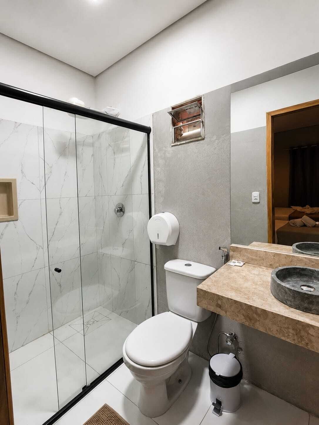 A modern bathroom with a glass shower enclosure, a toilet, a sink with a marble basin, and a mirror.