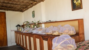 Ein Zimmer mit einer hölzernen Bank, einem Bett mit floralem Überwurf, einer reetgedeckten Decke und einem an der Wand befestigten Wappen.