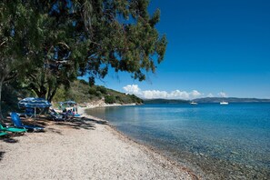 En strand med klart vatten, några båtar och parasoller.