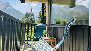 A balcony with a view of mountains, a green chair, a striped lounge chair, and a small table with a plant. - Terrace, balcony, parking, 28m², Serre Chevalier (Le Monêtier-les-Bains)