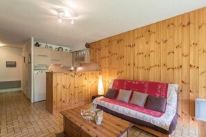 A cozy room with a wooden wall, a sofa, a coffee table, and a kitchen area with cabinets and a refrigerator.