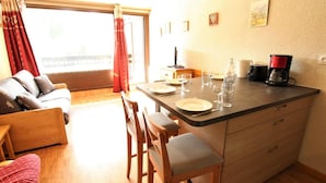 Ein gemütliches Wohnzimmer mit einer Couch, einem Esstisch für zwei Personen und einer Küchenzeile mit Kaffeemaschine.