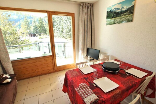 A dining area with a red tablecloth, a TV, and a scenic view through the glass door. - 50m from ski slopes, 2nd floor, swimming pool, balcony, 42m², Serre Chevalier (SERRE CHEVALIER)