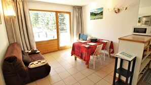 Ein gemütliches Wohnzimmer mit einer Couch, einem Esstisch mit rotem Tischläufer und einer Küchenzeile mit einer Mikrowelle.