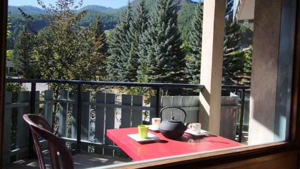Ein Balkon mit einem roten Tisch, einem Stuhl und einem Wasserkocher.