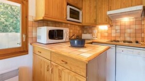 Una cocina compacta con armarios de madera, microondas, estufa y lavavajillas.