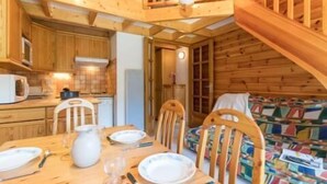 Una cabaña de madera acogedora con comedor, cocina y habitación doble con un edredón colorido.