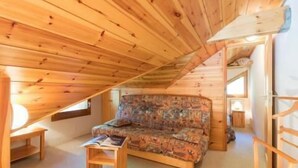 Una habitación cálida en el ático, con vigas de madera, un sofá estampado y una pequeña mesa.