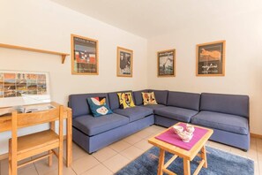 Un salon moderne avec un canapé bleu, une table d’appoint en bois et une table basse. Des tableaux encadrés ornent le mur et un livre est posé sur la table d’appoint.