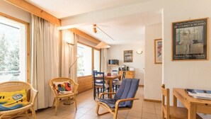 Ein gemütliches Wohnzimmer mit Korbmöbeln, ein Essbereich mit Holztischen und eine Küche im Hintergrund.
