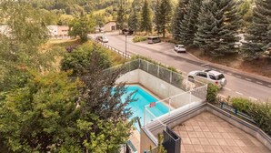 Ein Schwimmbecken mit umzäuntem Deck, umgeben von Bäumen und einer Straße mit Fahrzeugen.