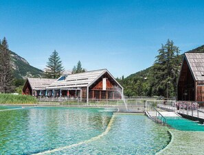 Un bâtiment rustique en bois, avec une piscine devant, entouré de montagnes et d’arbres.