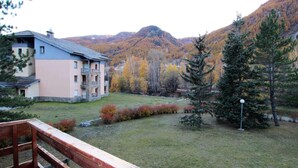 A building with a balcony, a grassy yard, and a mountainous backdrop.