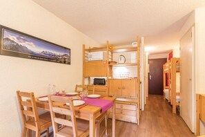 Una habitación compacta con una mesa de comedor de madera dispuesta para cuatro personas, un microondas, una tetera y un mueble pequeño. Un cuadro enmarcado cuelga en la pared.