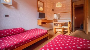 A small, cozy room with two single beds, a wooden desk with a chair, a television, and a mirror. - 300m from resort center, 2nd floor, view ski slopes, balcony, tv, ski locker, 27m², Valmorel (Valmorel)