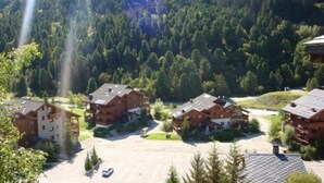 A mountain lodge with multiple wooden buildings, a parking area, and a forested backdrop. - 175m from shops, 3rd floor, view mountain, balcony, tv, 60m², Méribel-Mottaret (Méribel - Les Allues)