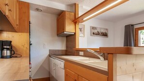 A compact kitchen with wooden cabinets, a built-in dishwasher, and a coffee machine. - 175m from shops, 3rd floor, view mountain, balcony, tv, 60m², Méribel-Mottaret (Méribel - Les Allues)