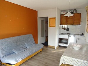 Un ambiente compatto con divano, tavolo da pranzo, angolo cottura e una porta che conduce a un'altra stanza.
