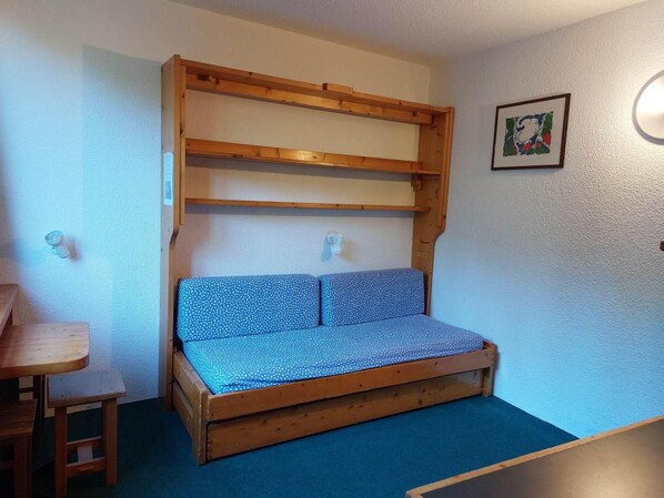 A small room with a wooden bunk bed, a blue sofa, a wooden table, and a framed picture on the wall.