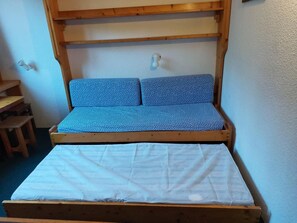 A small, wooden bed with a white mattress and blue polka-dotted bedding.