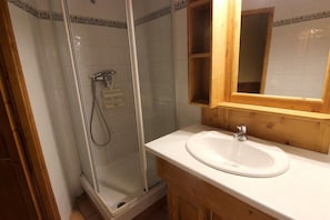 Een badkamer met een douchecabine van glas, een houten wastafelmeubel met een wastafel en een spiegel erboven.