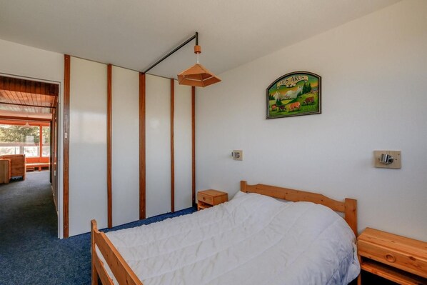 A bedroom with a wooden bed, a nightstand, a wall-mounted light fixture, and a framed picture of a landscape.