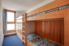 Een slaapkamer met stapelbed, een raam, een blauw tapijt en een geruit kussen.