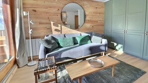 A modern living room with a wooden wall, a round mirror, a sofa with patterned cushions, a coffee table, and a radiator. - 10m from ski slopes, 1st floor, balcony, 35m², Méribel-Mottaret (Méribel - Les Allues)