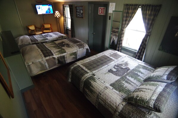 A room with two beds, a television, a chair, and an exit sign.