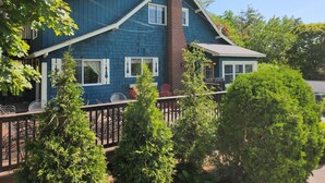 A two-story house with a blue exterior, a brick chimney, and a porch with outdoor furniture. - Lake George 5 Bed/ 3 Bath home w/ lake & resort access (Lake George)